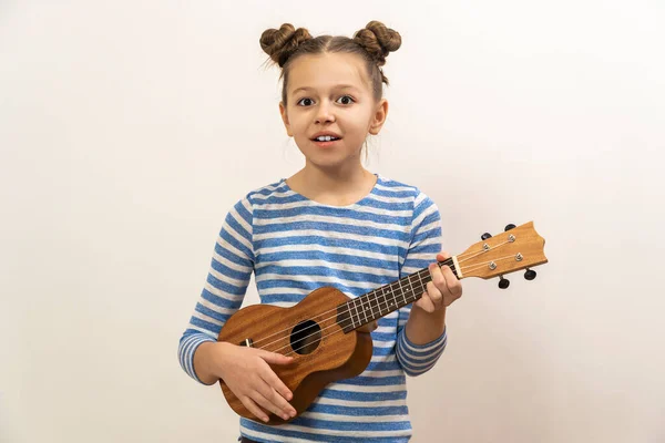 Lány sötét haj játszik gitár ukulele egy világos háttér. — Stock Fotó