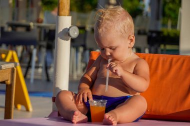 Sarı saçlı küçük çocuk, güneşlenir ve meyve suyu içer..