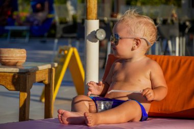 Sarı saçlı küçük çocuk, güneşlenir ve meyve suyu içer..