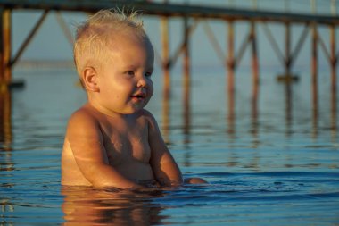 Sarı saçlı küçük çocuk, denize otur ve gül..