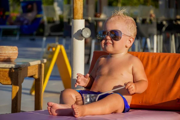 Sarı saçlı küçük çocuk, güneşlenir ve meyve suyu içer..