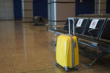 Sarı bavul havaalanında boş koltukların yanında duruyor.