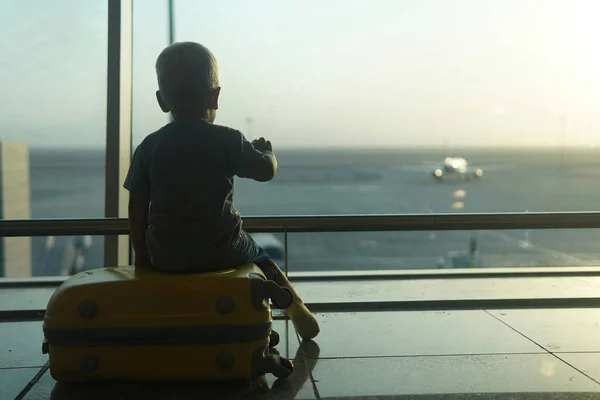 Маленький Мальчик Сидит Желтом Чемодане Аэропорту Смотрит Самолет — стоковое фото
