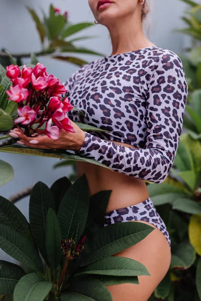 pretty caucasian woman with perfect fit body in leopard swimsuit with tropical beautiful flowers