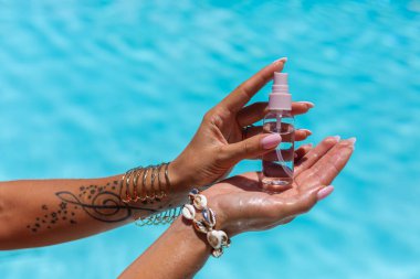 Kadınların elleri mavi yüzme havuzunun arka planında küçük bir şişe bronzlaşma yağı tutuyor..