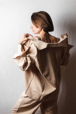 Gri beyaz arka planda beyaz dantelli sutyen ve bej takım elbiseli büyük göğüslü güzel bir kadının portresi.  