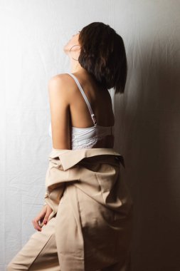 Gri beyaz arka planda beyaz dantelli sutyen ve bej takım elbiseli büyük göğüslü güzel bir kadının portresi.  