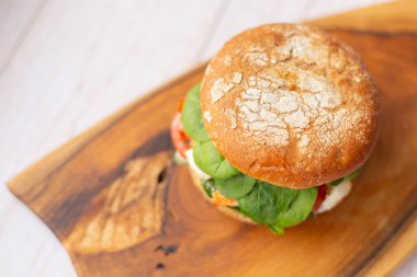 Tahta bir tahtanın üzerinde, Kral karidesli, feta peynirli ve sebzeli hamburger.