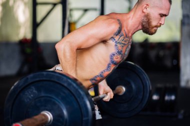 Spor salonunda sakallı, güçlü bir adam dövmesi var. Halter egzersizi yapan kaslı vücut geliştirici.
