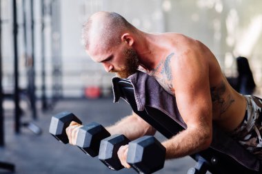 Genç, kaslı, güçlü, kaslı, sakallı Avrupalı adam omuzları için halterlerle sıkı egzersiz yapıyor.