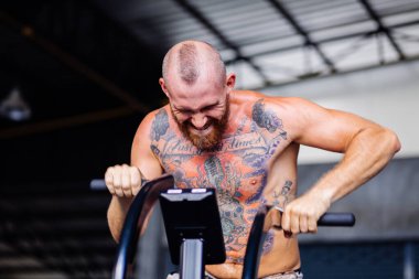 Avrupalı yakışıklı, kaslı, sakallı, spor salonunda bisiklet süren adam.