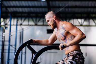 Avrupalı yakışıklı, kaslı, sakallı, spor salonunda bisiklet süren adam.