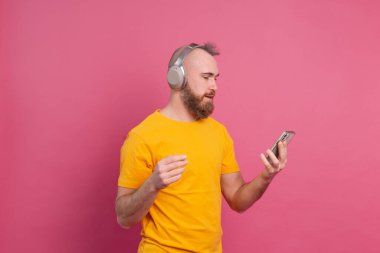 Sıradan müzik dinleyen yakışıklı adam pembe arka planda izole edilmiş kulaklıklı.