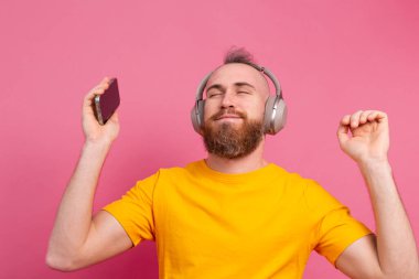 Pembe arka planda izole edilmiş cep telefonu ve kulaklığı olan sıradan dans eden yakışıklı adam.