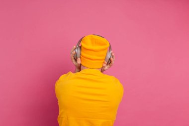 Pembe arka planda izole edilmiş kulaklıklarla dans eden yakışıklı adam.