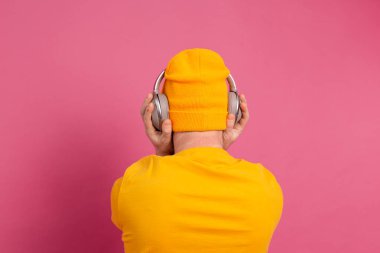 Pembe arka planda izole edilmiş kulaklıklarla dans eden yakışıklı adam.