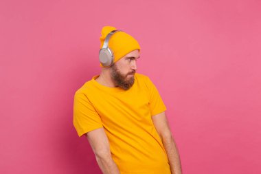 Sıradan müzik dinleyen yakışıklı adam pembe arka planda izole edilmiş kulaklıklı.