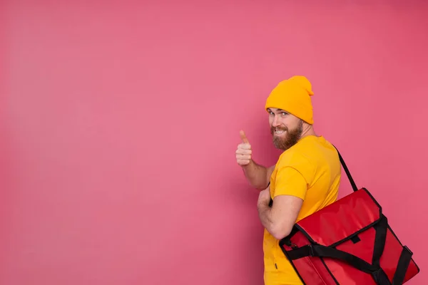 European bearded delivery man with box with food smiling and showing thumb up on pink background isolated