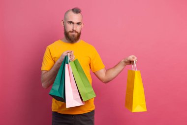 Mutlu sakallı, sıradan görünüşlü, renkli alışveriş çantaları olan, stüdyo pembe arka planlı, mutlu bir adam.