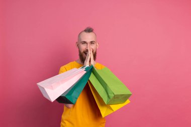 Mutlu sakallı, sıradan görünüşlü, renkli alışveriş çantaları olan, stüdyo pembe arka planlı, mutlu bir adam.