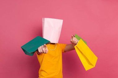 Strong muscle man casual look with colorful shopping bags cover head with bag studio pink background