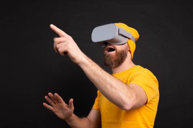 Handsome positive bearded man touching air in vr glasses studio background