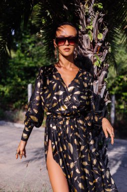 İnce, bronz tenli, kısa siyah saçlı, bronz, palmiye ağacıyla süslenmiş, siyah altın sarısı uzun pelerinli bir kadının egzotik portresi.