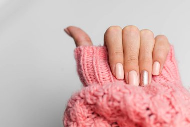 Pretty nude color manicure, one finger shiny golden, on knitted pink wool pillover backgroun