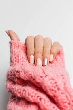 Pretty nude color manicure, one finger shiny golden, on knitted pink wool pillover backgroun