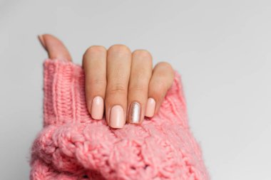 Pretty nude color manicure, one finger shiny golden, on knitted pink wool pillover backgroun