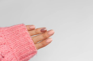 Pretty nude color manicure, one finger shiny golden, on knitted pink wool pillover backgroun