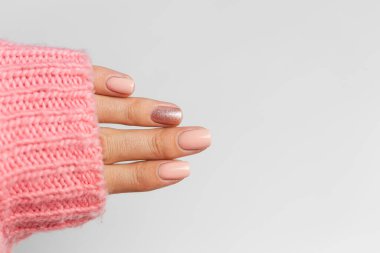 Pretty nude color manicure, one finger shiny golden, on knitted pink wool pillover backgroun