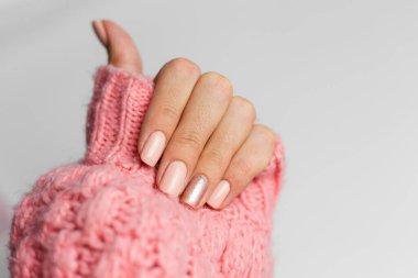 Pretty nude color manicure, one finger shiny golden, on knitted pink wool pillover backgroun