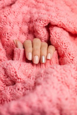 Pretty nude color manicure, one finger shiny golden, on knitted pink wool pillover backgroun
