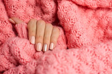 Pretty nude color manicure, one finger shiny golden, on knitted pink wool pillover backgroun