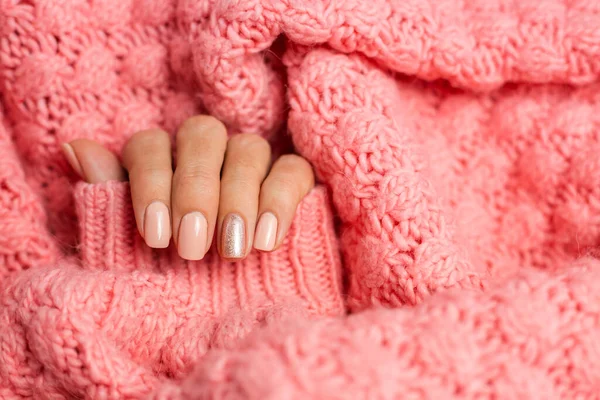 Pretty nude color manicure, one finger shiny golden, on knitted pink wool pillover backgroun