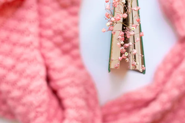 Green book with dry flowers on a pink warm knitted sweater background