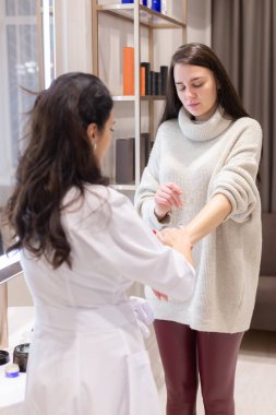 Two women, a beautician doctor and a client, stand at the mirror, for a consultation, the doctor applies cream to the woman's hands and makes a light massage