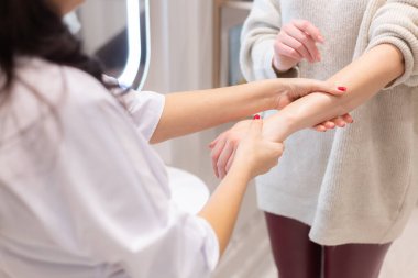 Two women, a beautician doctor and a client, stand at the mirror, for a consultation, the doctor applies cream to the woman's hands and makes a light massage
