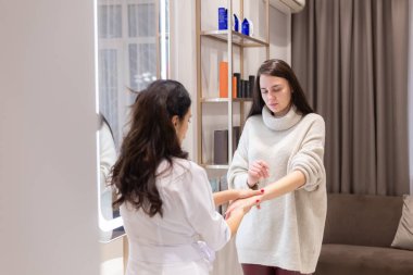 Two women, a beautician doctor and a client, stand at the mirror, for a consultation, the doctor applies cream to the woman's hands and makes a light massage