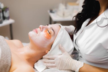 Kozmetoloji odasındaki bir güzellik salonunda genç bir kız yatağında maskeyle uzanıyor ve gözlerinin altında yamalar var.