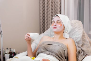 Kozmetoloji odasındaki bir güzellik salonunda genç bir kız yatağında maskeyle uzanıyor ve gözlerinin altında yamalar var.