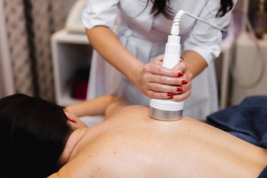 Spa salonundaki kız sırt ve boyun masajı yaptırıyor, kozmetoloji masasında uzanıyor, rahatlıyor ve bu süreçten zevk alıyor.