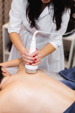 Spa salonundaki kız sırt ve boyun masajı yaptırıyor, kozmetoloji masasında uzanıyor, rahatlıyor ve bu süreçten zevk alıyor.