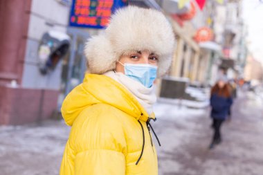 Soğuk bir günde kışın giyinmiş bir kadın otobüs durağında otobüs bekliyor.
