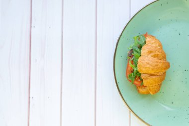 Tahta bir masada seramik tabakta roket salatası ve sebzeli kruvasan.