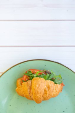 Tahta bir masada seramik tabakta roket salatası ve sebzeli kruvasan.