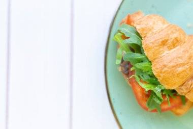Tahta bir masada seramik tabakta roket salatası ve sebzeli kruvasan.
