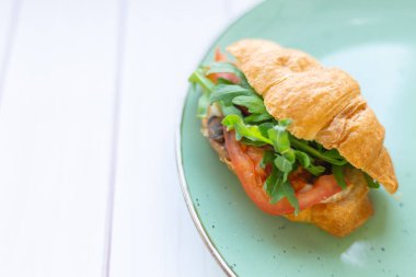 Tahta bir masada seramik tabakta roket salatası ve sebzeli kruvasan.