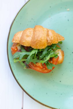 Tahta bir masada seramik tabakta roket salatası ve sebzeli kruvasan.